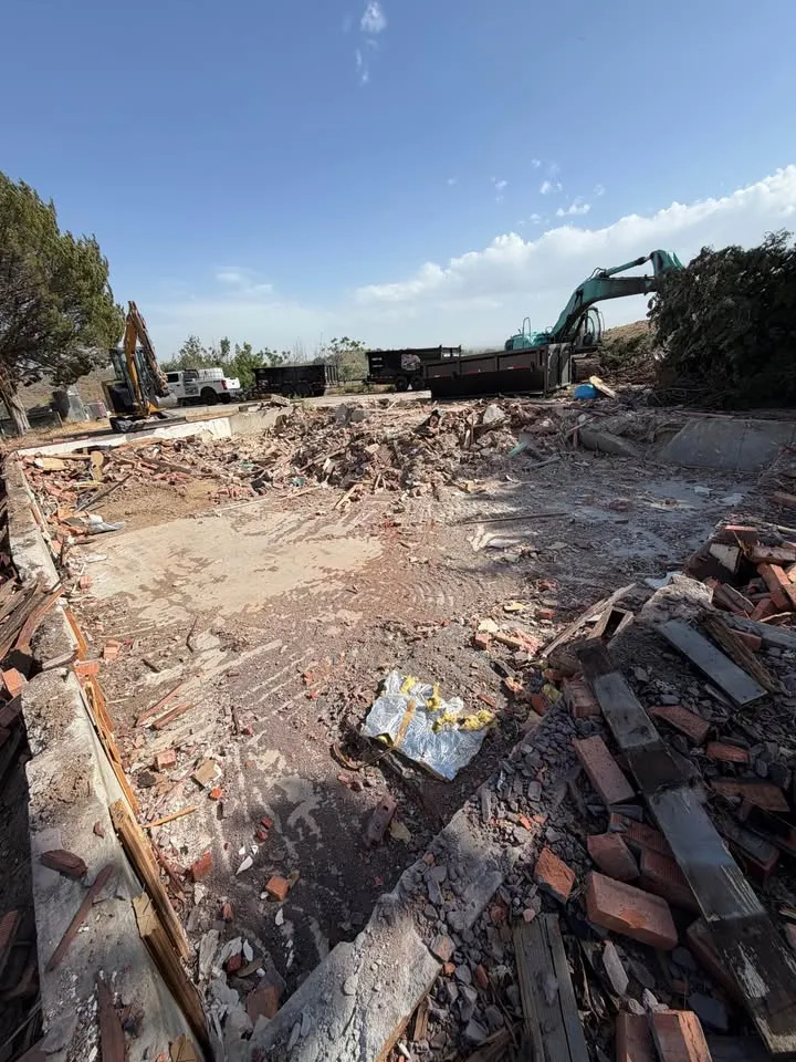 Excavator working across the brick and timber rubble of a house that has been taken down to its foundation